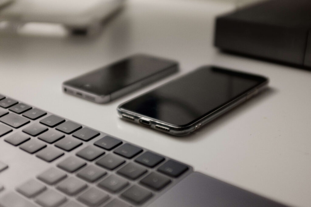 A White Table with Two Cell Phones and a Keyboard.