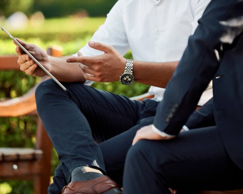 Two Businessmen Review Notes on a Tablet in the Courtyard.